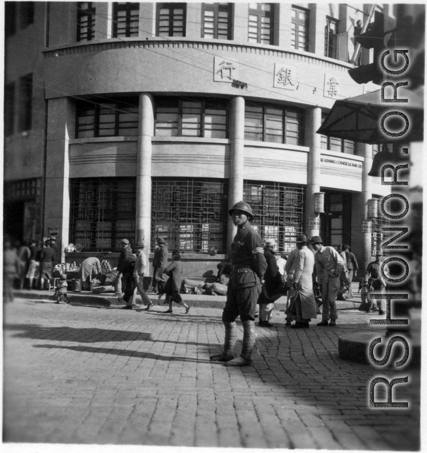 Scenes around Kunming city, Yunnan province, China, during WWII: Street corner with a stern traffic cop and the "Kunming Commercial Bank, Ltd."