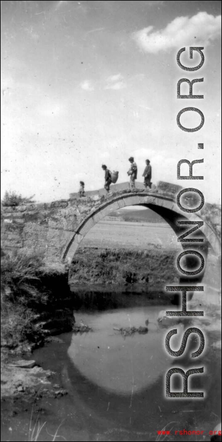 Chinese pedestrians cross arched stone bridge in SW China during WWII.
