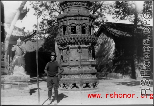 A westerner stands in front of a large incense burner in a temple in China during WWII.