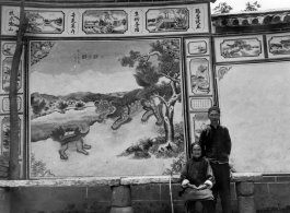 An elderly woman and man pose before a traditional decorative painted wall in SW China during WWII.