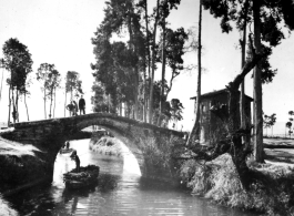 A boat on a canal near a small bridge in rural Yunnan province, China, with American GIs looking on from bridge above. During WWII.