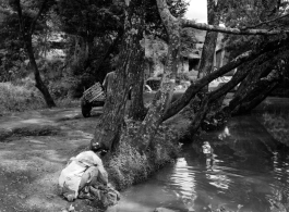 Local people in a village in Yunnan province, China: A woman washes clothes in a tree-shaded village pond. During WWII.
