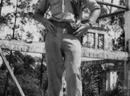 Bob Riese poses amongst remains of aircraft factory and hangers at the air base at Liuzhou, in 1945. The facilities at the base were first destroyed by the Chinese and Americans during retreat in the face of Ichigo during the fall of 1944, then may have been destroyed more by American bombardment during Japanese occupation, and possibly destroyed more by the Japanese as they retreated the area in 1945.