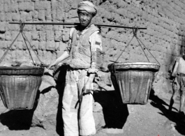 Rural worker with baskets on a shoulder pole. Local people in China, probably in Yunnan province during WWII.