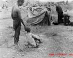 A gravely ill boy is supported by an adult: The sick and weakened during the Chinese civilian evacuation in Liuzhou city Guangxi province, China, during WWII, during the summer or fall of 1944 as the Japanese swept through as part of the large Ichigo push.