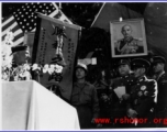 Burma Road dedication ceremony in Kunming, China, on February 4, 1945, during WWII. Review of first convoy (or one of the first convoys) to reach China. General view of the stage and reviewing party, with American and Chinese dignitaries, soldiers, and civilian VIPs. An American band plays, and an honor lines on both sides of the center carpet stand in formation.  Official dignitaries at the ceremony included, on the Chinese side, such figures as General Lung Yun, Governor of Yunnan Province,  Gen. Wang Yu-
